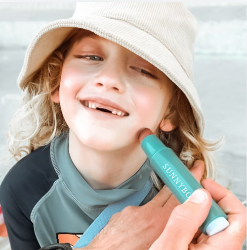 Using a sunscreen applicator to apply sunscreen quickly and easily to a smiling boys face, without the mess.
